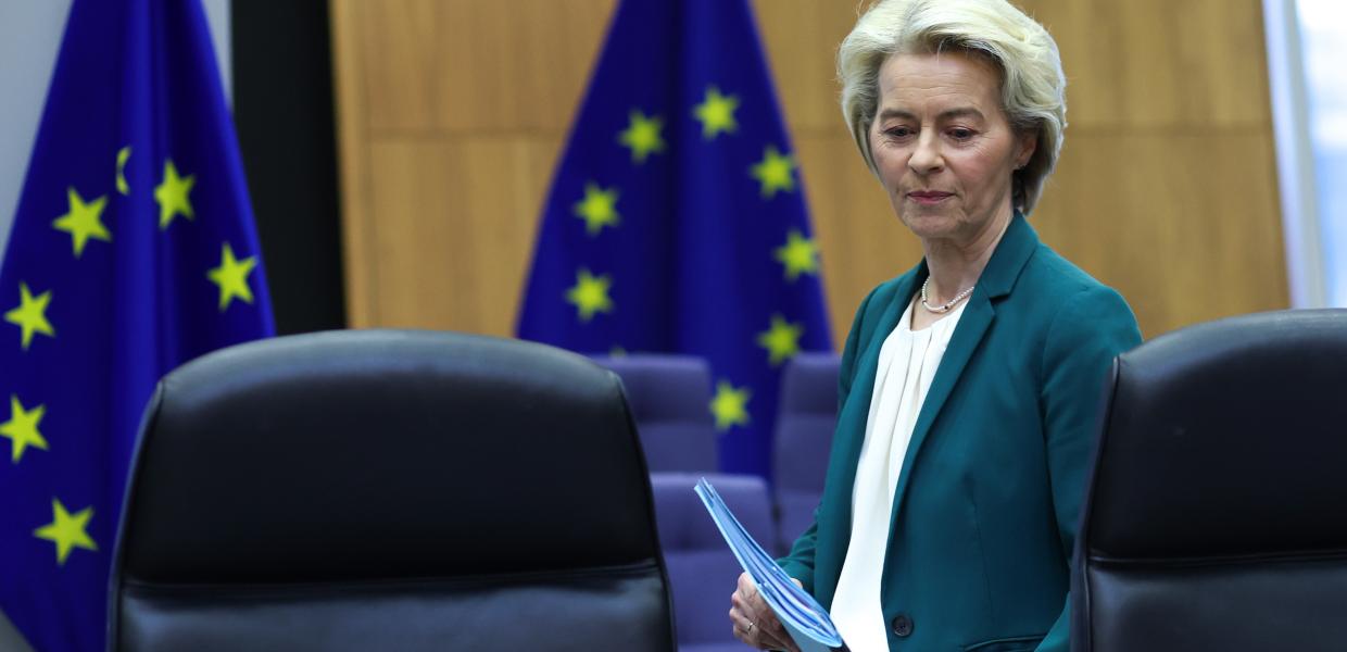 η Ούρσουλα φον ντερ Λάιεν με φάκελο στο χέρι και πίσω της σημαίες της ΕΕ