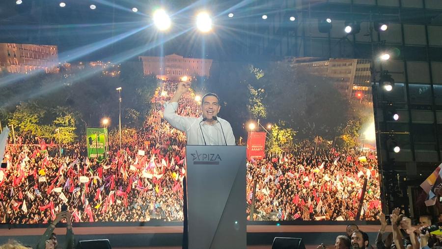 Ο Τσίπρας μιλάει με την οθόνη πίσω του να δείχνει το πλήθος κόσμου
