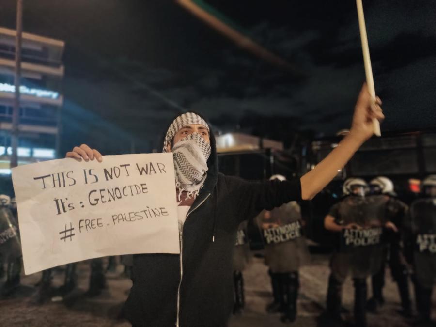 Νεαρός με χαρτόνι που γράφει δεν είναι πόλεμος, είναι γενοκρονία