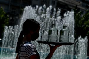 Σερβιτόρα με μάσκα κρατάει δίσκο με νερό.