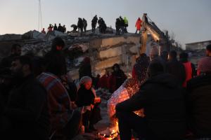 Άνθρωποι γύρω από τη φωτιά κοντά σε χαλάσματα από τον σεισμό
