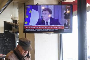 Τηλεόραση δείχνει τον Μακρόν να μιλά ενώ ένας παππούς περνά μπροστά