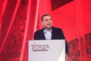 Ο Αλέξης Τσίπρας μιλά στο μικρόφωνο από το βήμα με το λογότυπο του ΣΥΡΙΖΑ