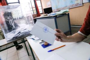 χέρι κρατά φάκελο και πίσω η κάλπη και η έδρα