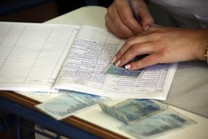 Χέρια γυναίκας με εκλογικούς καταλόγους και ταυτότητες πάνω σε θρανίο