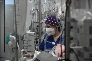 Γιατρός με μάσκα και σκουφάκι σε ΜΕΘ νοσοκομείου ανάμεσα σε μηχανήματα