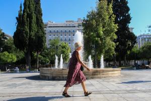 Γυναίκα με καπέλο περπατά μπροστά από το σιντριβάνι στο Σύνταγμα