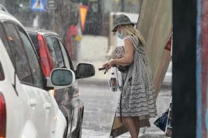 Γυναίκα μέσα στη βροχή με καπέλο προχωρά δίπλα σε αυτοκίνητα