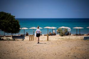 κοπέλα σε σακούλα και καφέ στο χέρι πάει προς θάλασσα με ομπρέλες και ξαπλώστρες