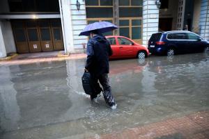 Άντρας με ομπρέλα περπατά σε δρόμο που έχει γεμίσει νερά από την βροχή
