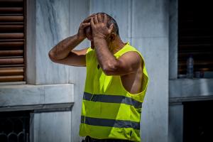 Εργάτης με κίτρινο γιλέκο έχει τα χέρια στο κεφάλι του λόγω της ζέστης