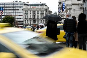 Άνθρωποι στο κέντρο της Αθήνας και ταξί που περνούν μπροστά
