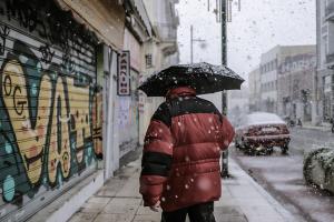 Άντρας με χοντρό μπουφάν και ομπρέλα περπατά σε δρόμο την ώρα που χιονίζει