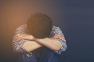 νεαρό αγόρι καθισμένο με το πρόσωπο στα γόνατά του