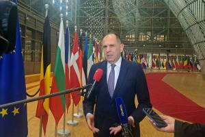 Ο Γεραπετρίτης στις Βρυξέλλες μιλά σε μικρόφωνα δημοσιογράφων και πίσω του οι σημαίες χωρών της ΕΕ