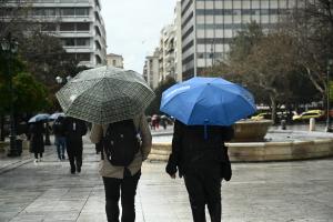 Δύο ανθρωποι με ομπρέλες γυρισμένοι πλάτη περπατούν στην πλατεία Συντάγματος