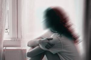 Θολή φωτογραφία γυναίκας να κάθεται σε κρεβάτι με τα χέρια στα γόνατά της και να κοιτά προς το παράθυρο
