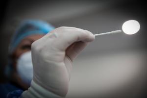 Γιατρός με στολή δείχνει στον φακό μπατονέτα για λήψη δείγματος για κορωνοϊό