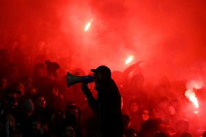 Οπαδοί σε εξέδρα σε κόκκινο φόντο από φωτοβολίδες