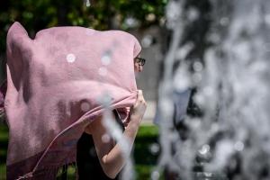 Γυναίκα σκεπασμένη με μαντήλι στο κεφάλι περνά μπροστά από συντριβάνι