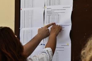 χέρια στα χαρτιά που δείχνουν τις βάσεις για τις Πανελλήνιες τοιχοκολλημένα έξω από σχολείο