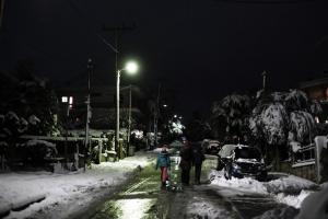 Γονείς με παιδί περπατούν σε χιονισμένο δρόμο τη νύχτα