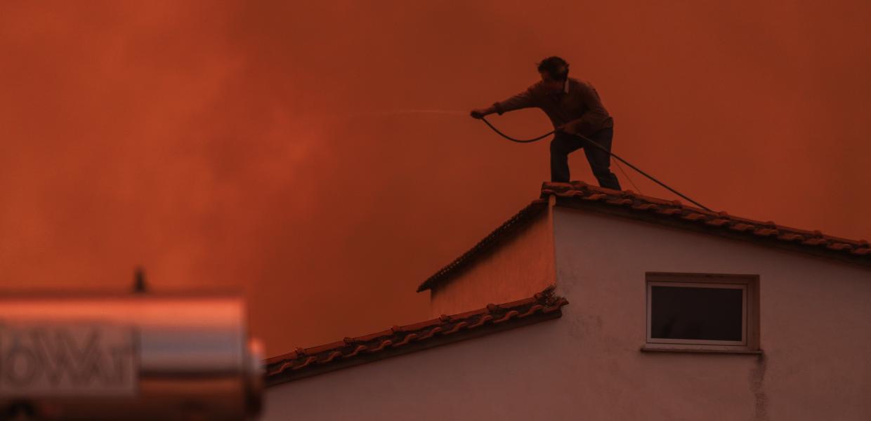 Στο χωριό Γούβες άνδρας σε σκεπή σπιτιού βοηθάει στην κατάσβεση της πυρκαγιάς που καίει επί μέρες τη Βόρεια Εύβοια.