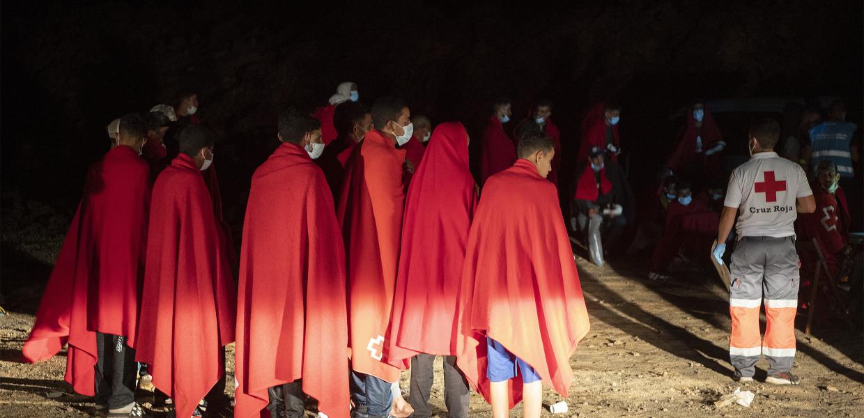Μετανάστες σκεπασμένοι με κόκκινες κουβέρτες του Ερυθρού Σταυρού