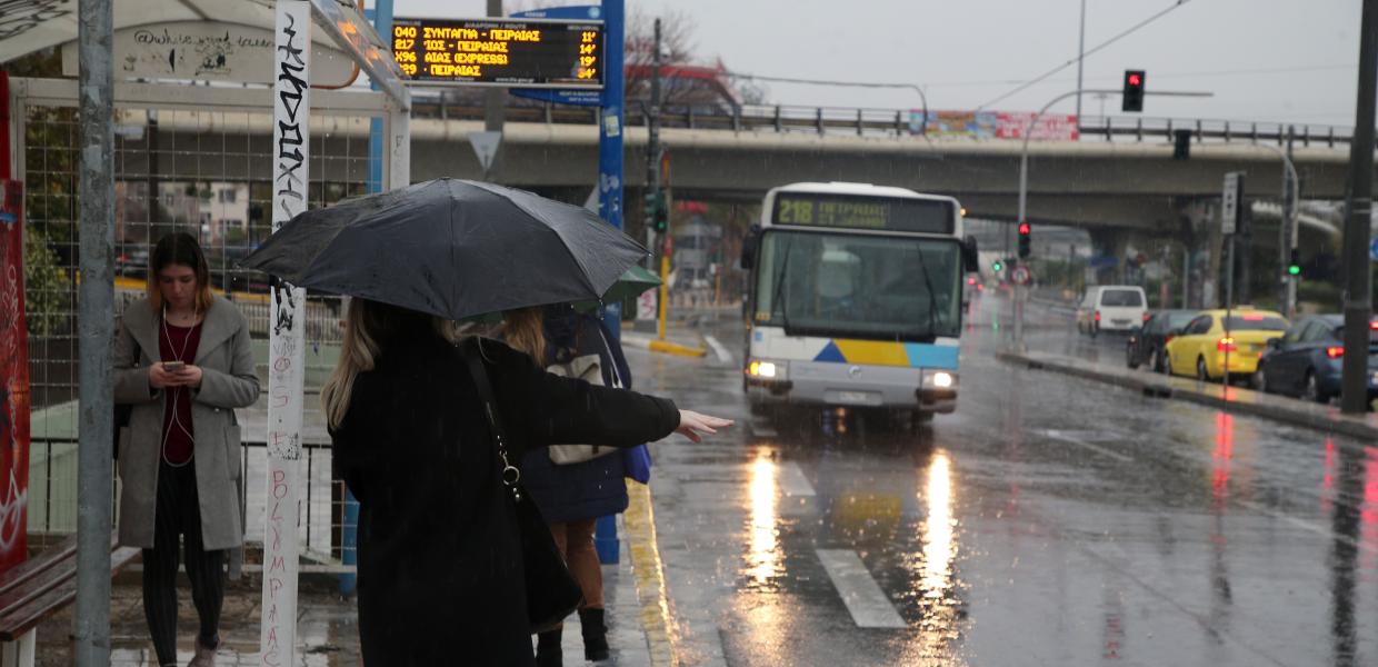 Άνθρωποι με ομπρέλες στη στάση λεωφορείου υπό βροχή