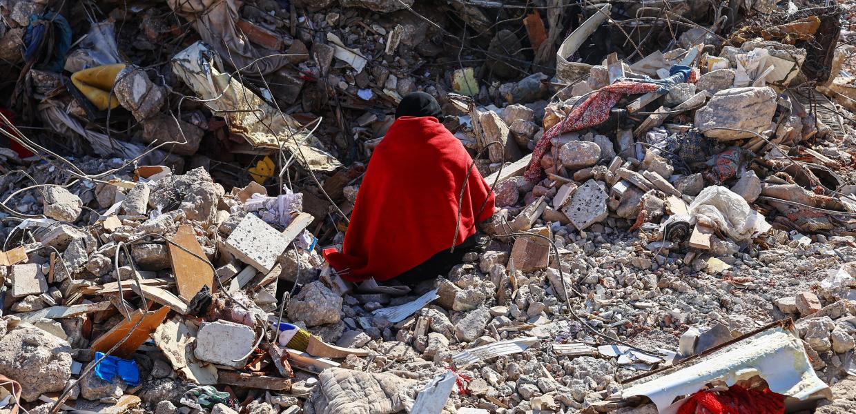 Μία γυναίκα τυλιγμένη με κουβέρτα κάθεται στα ερείπια του σπιτιού της που γκρεμίστηκε από τον σεισμό στην Τουρκία