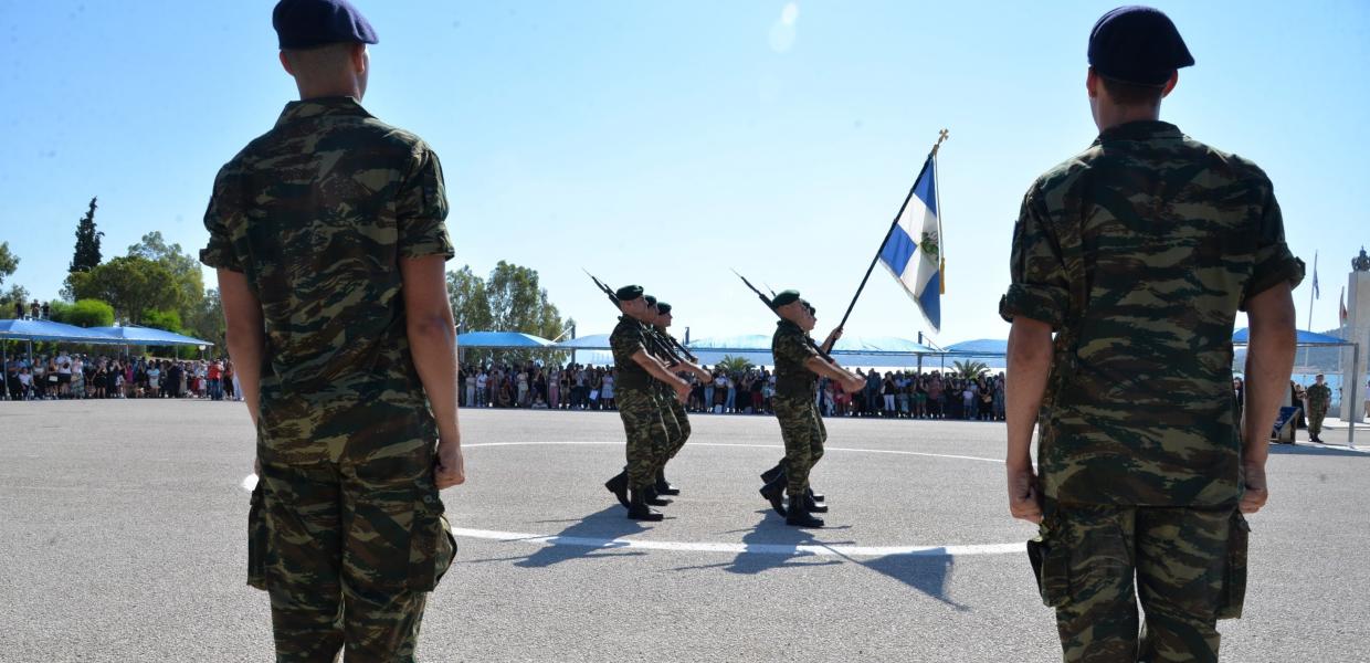 Στρατιώτες στέκονται προσοχή μπροστά από παρέλαση με ελληνική σημαία