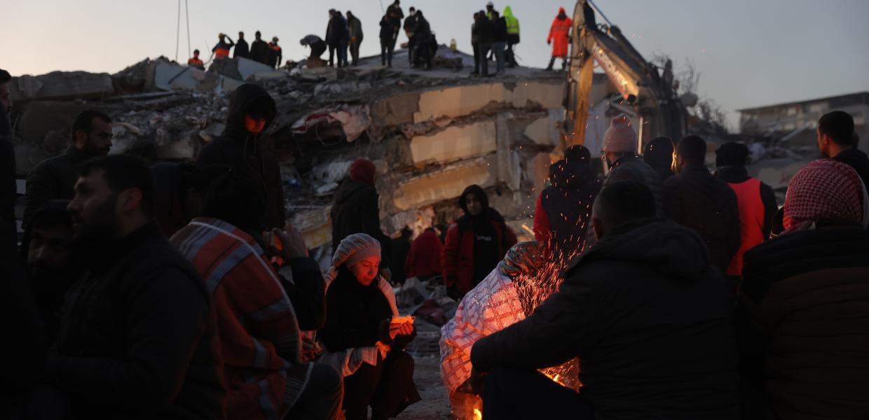 Άνθρωποι γύρω από τη φωτιά κοντά σε χαλάσματα από τον σεισμό