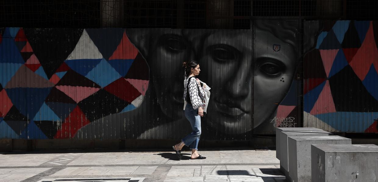 Κοπέλα περπατά σε πεζόδρομο μπροστά από γκράφιτι