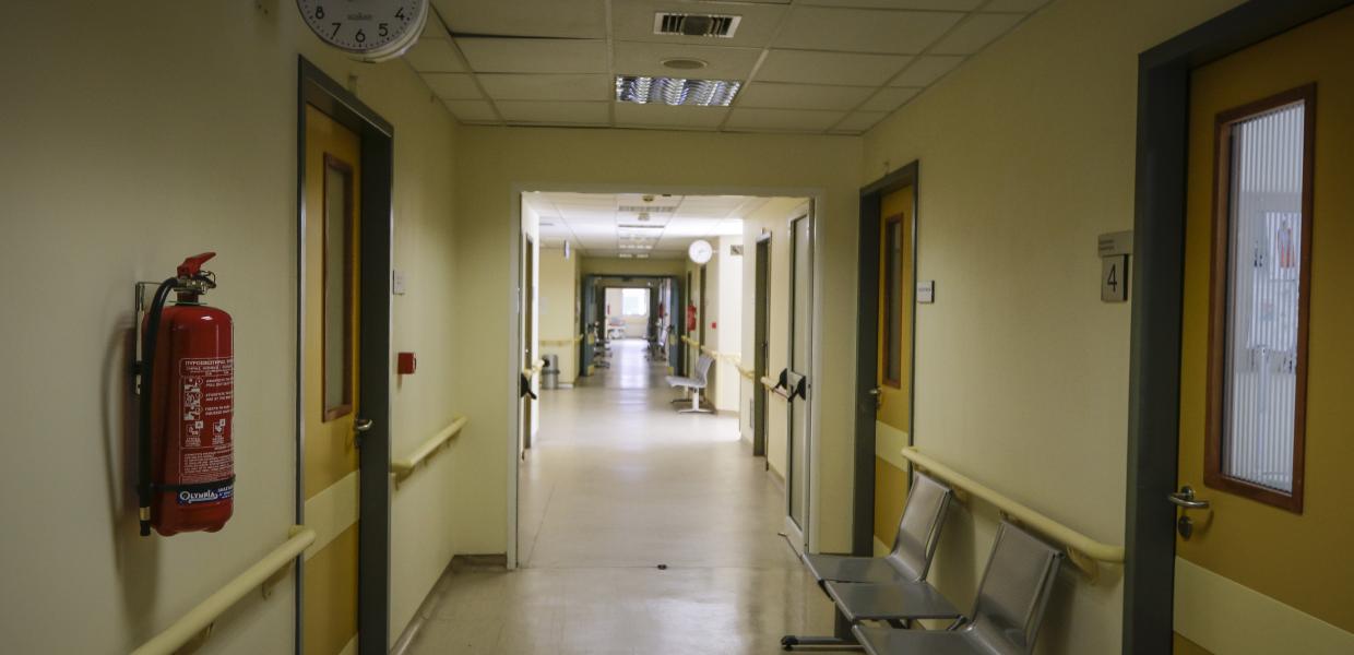 Άδειος διάδρομος νοσοκομείου με καρέκλες στα δεξιά, πόρτες και ένα πυροσβεστήρα αριστερά, στον τοίχο