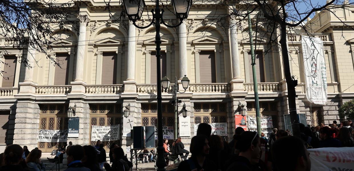 Κόσμος έξω από το κτίριο του Εθνικού Θεάτρου στην πρόσοψη του οποίου υπάρχουν πανό