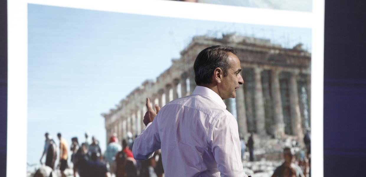 Ο Κυριάκος Μητσοτάκης γυρισμένος πλάτη μπροστά από γιγαντοοθόνη που δείχνει τον Παρθενώνα