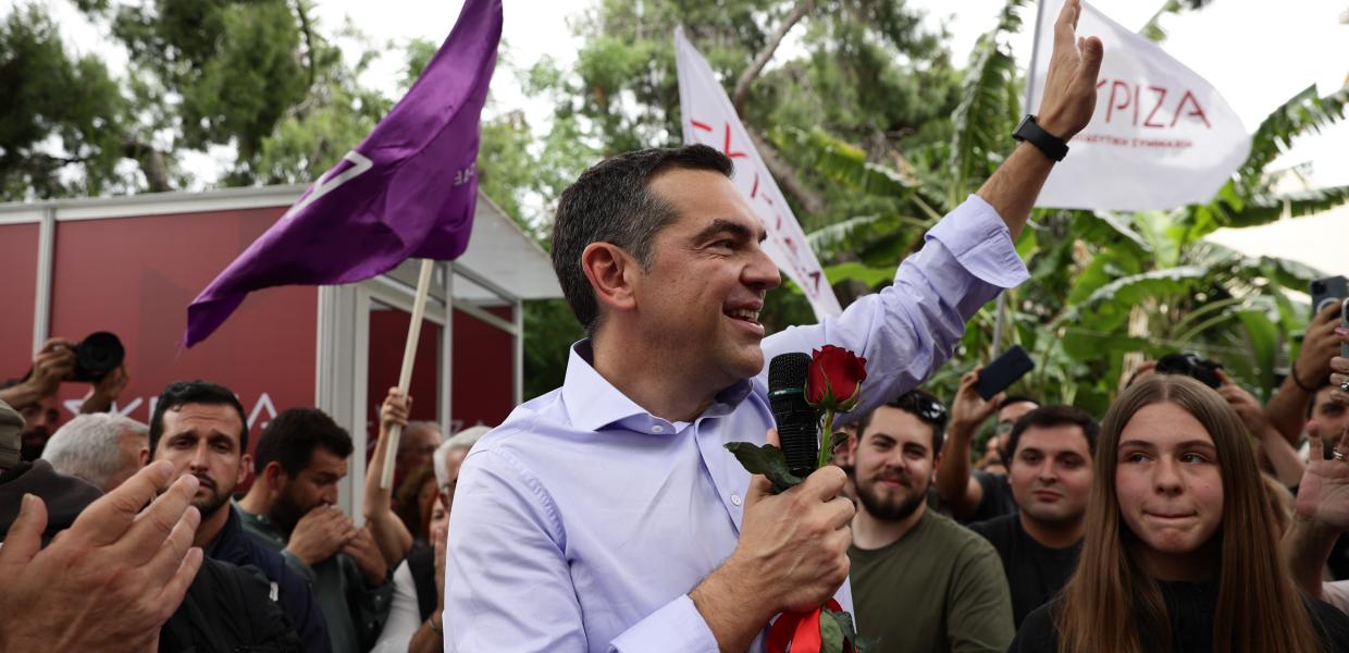 Ο Αλέξης Τσίπρας μιλά σε κόσμο με το μικρόφωνο και ένα λουλούδι στο χέρι