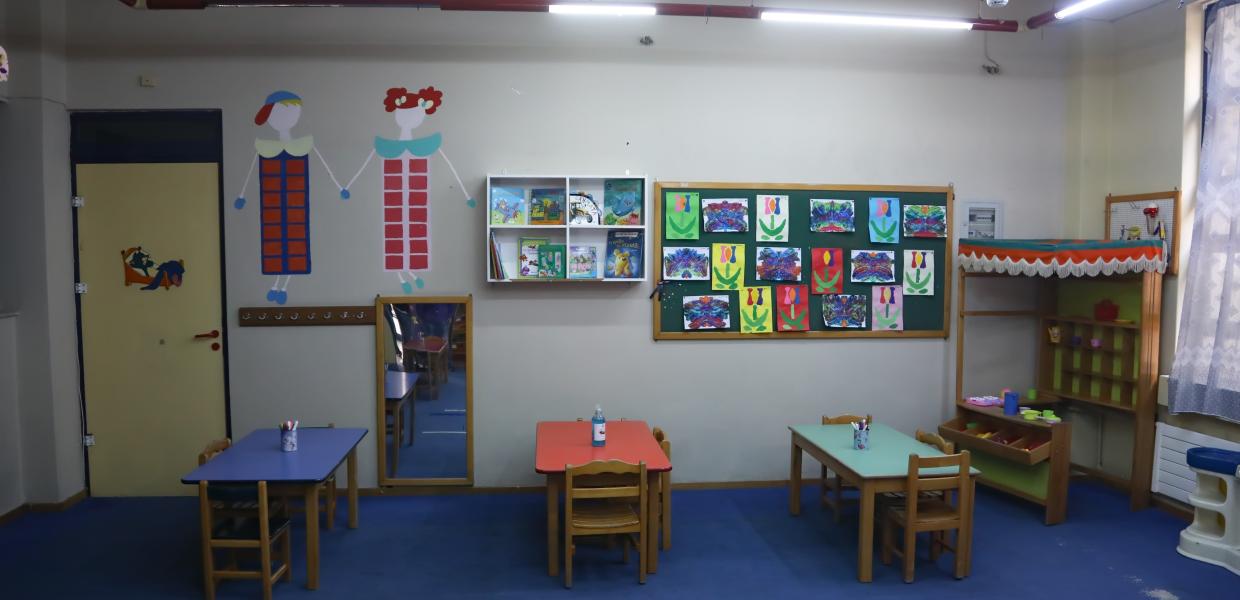 Αίθουσα βρεφονηπιακού σταθμού με τραπέζια και ζωγραφιές στους τοίχους
