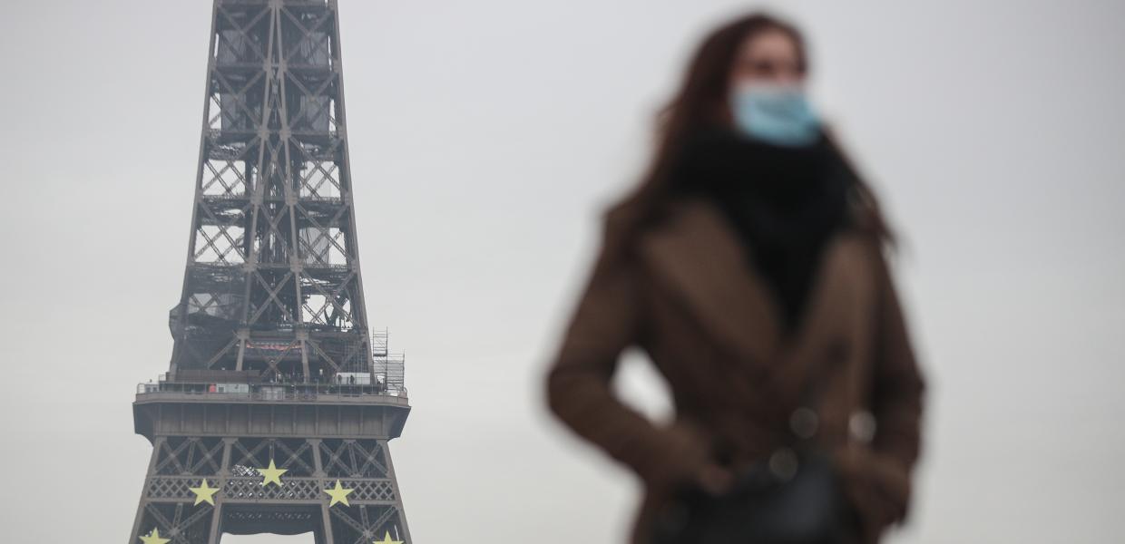 Κοπέλα με παλτό και μάσκα μπροστά από τον πύργο του Άιφελ 