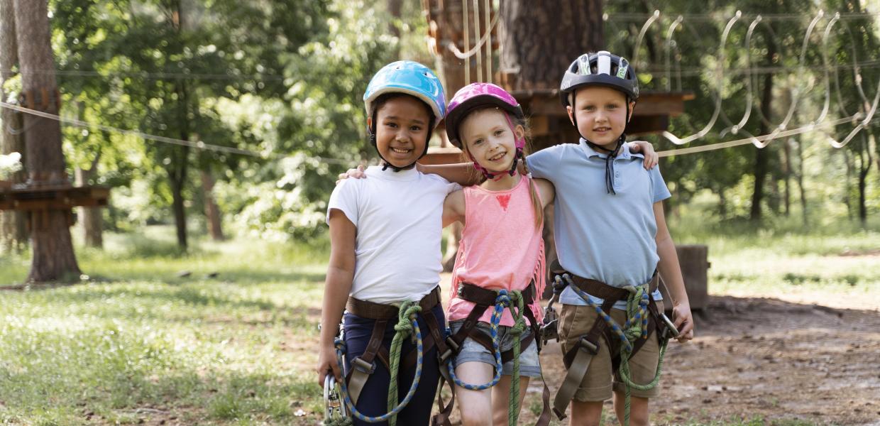 Τρία παιδιά ποζάρουν αγκαλιά με εξοπλισμό για αναρρίχηση 
