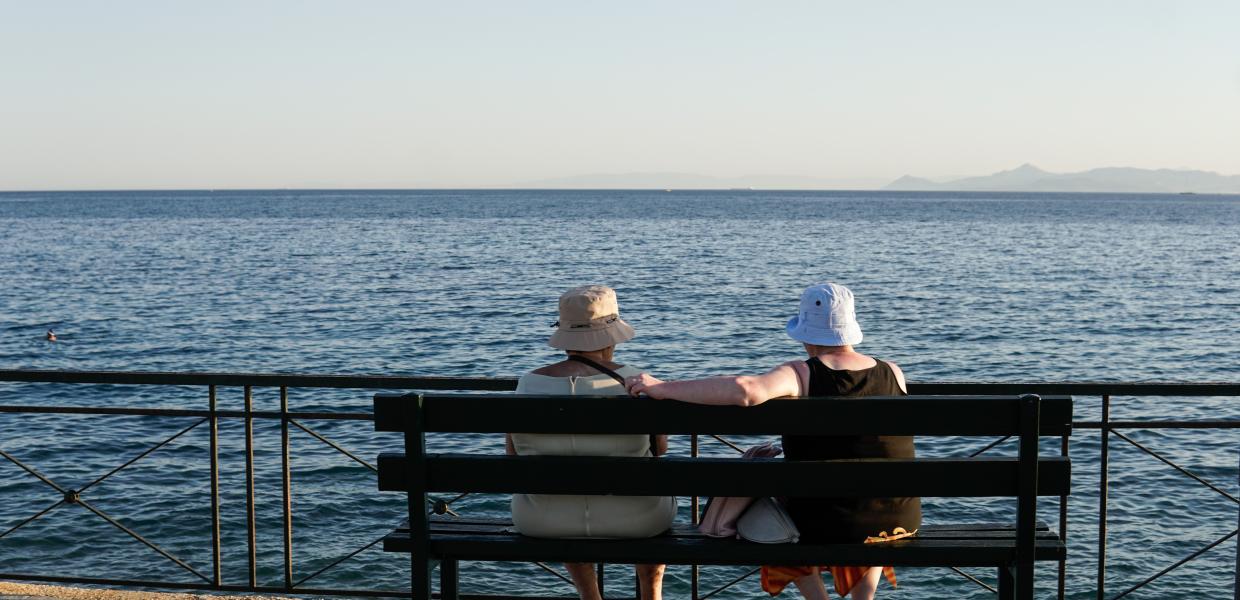Γιαγιάδες με καπέλα καθισμένες σε παγκάκι κοιτούν προς την θάλασσα