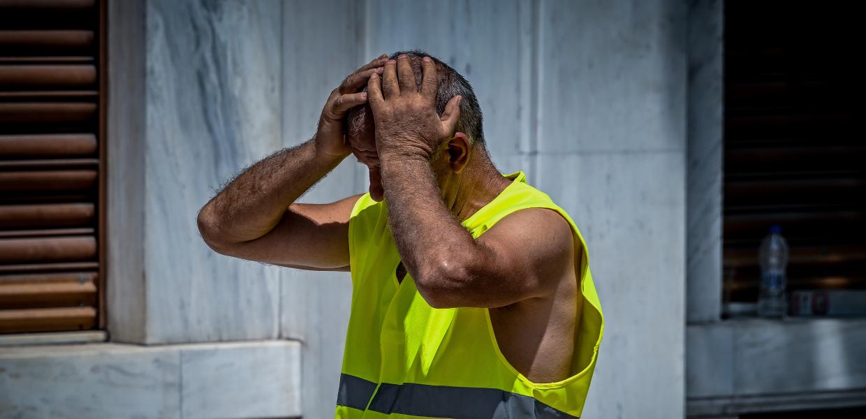 Εργάτης με κίτρινο γιλέκο έχει τα χέρια στο κεφάλι του λόγω της ζέστης