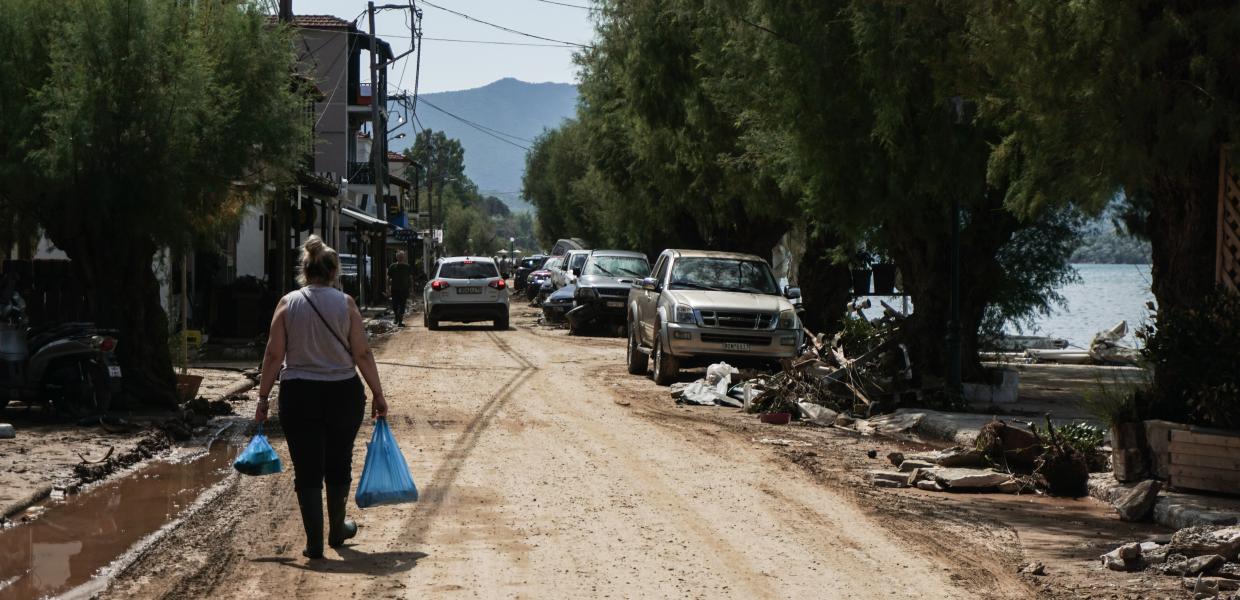 Γυναίκα με σακούλες στο χέρι περπατά σε κατεστραμμένο από την κακοκαιρία δρόμο