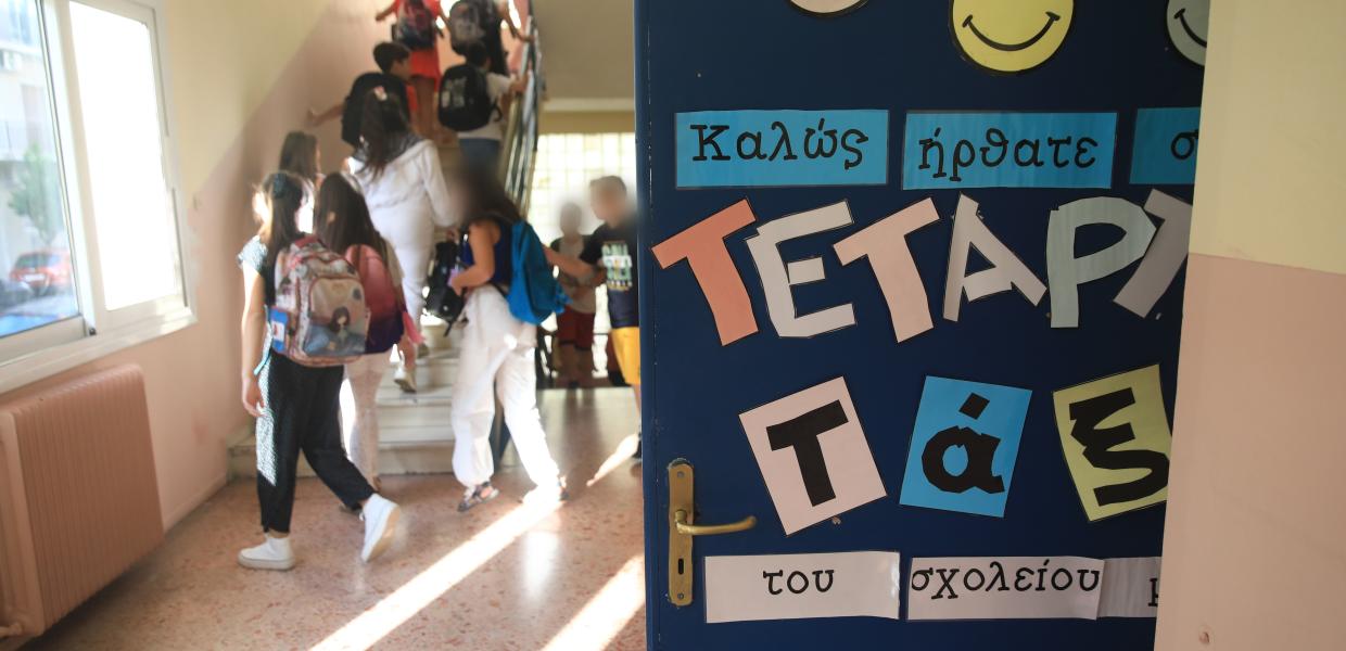 πόρτα τάξης με χαρτόνι που γράφει «καλως ήρθατε» και παιδιά πίσω να ανεβαίνουν τις σκάλες του σχολείου