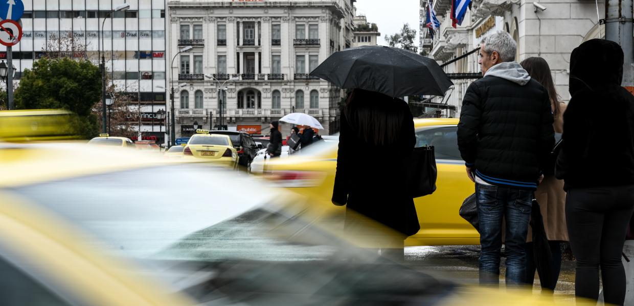 Άνθρωποι στο κέντρο της Αθήνας και ταξί που περνούν μπροστά
