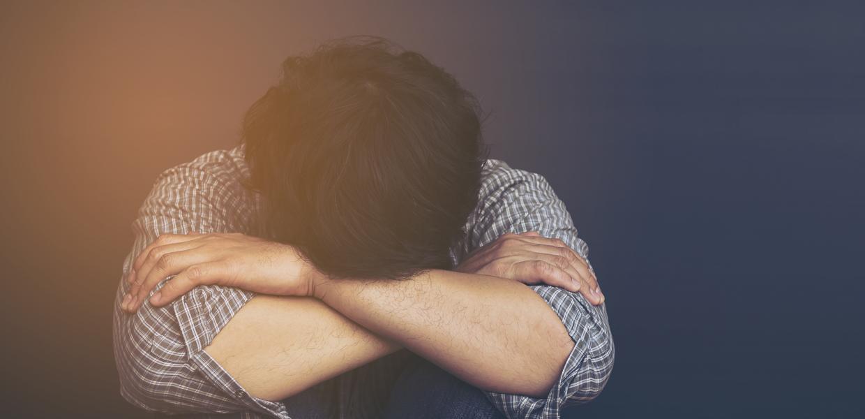 Αγόρι κάθεται σκυμμένο και καθιστό με το πρόσωπό στα πόδια του