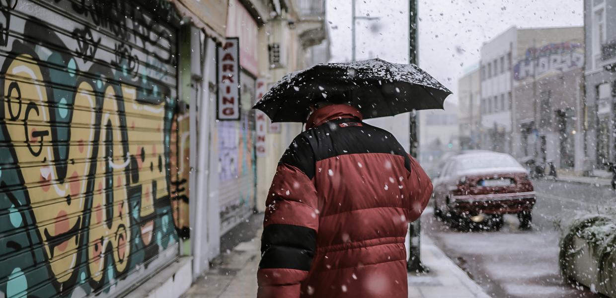 Άντρας με χοντρό μπουφάν και ομπρέλα περπατά σε δρόμο την ώρα που χιονίζει