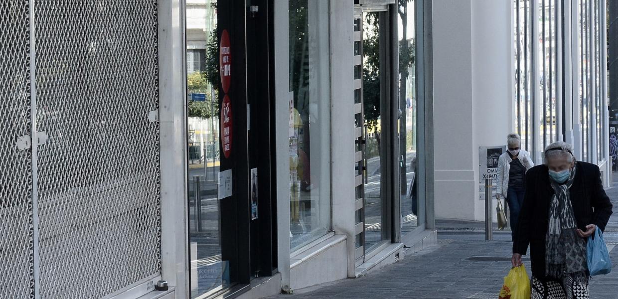 Ηλικιωμένη περπατά σε δρόμο του Πειραιά δίπλα από κλειστά και ανοιχτά καταστήματα