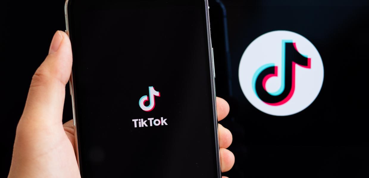 Λογότυπο του TikTok στο backround και σε οθόνη κινητού που κρατά χέρι