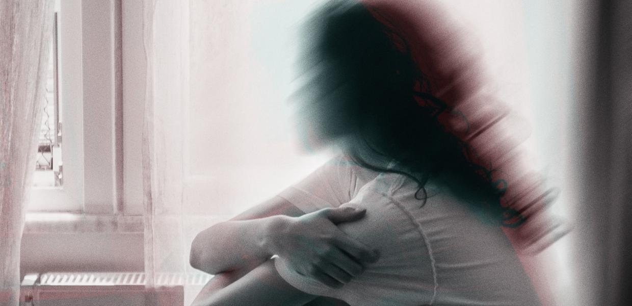 Θολή φωτογραφία γυναίκας να κάθεται σε κρεβάτι με τα χέρια στα γόνατά της και να κοιτά προς το παράθυρο